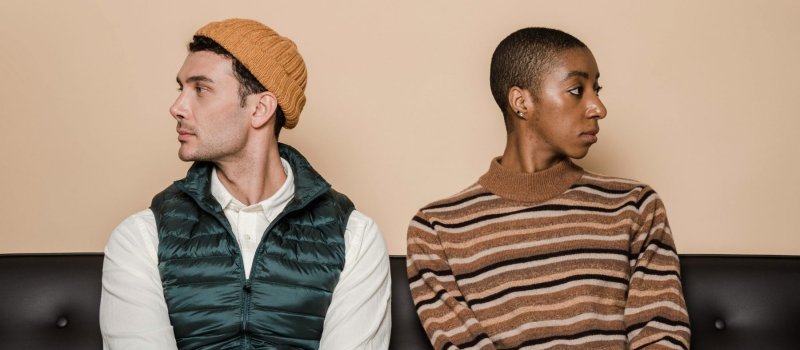 Black woman and white man sitting on a sofa, facing away from each other, showing distance and avoidance