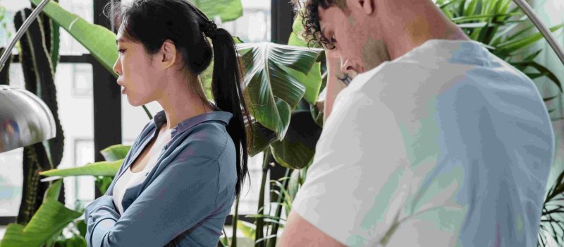 Asian woman and a man standing apart, both looking upset and defensive - representing emotional triggers and conflict in relationships.